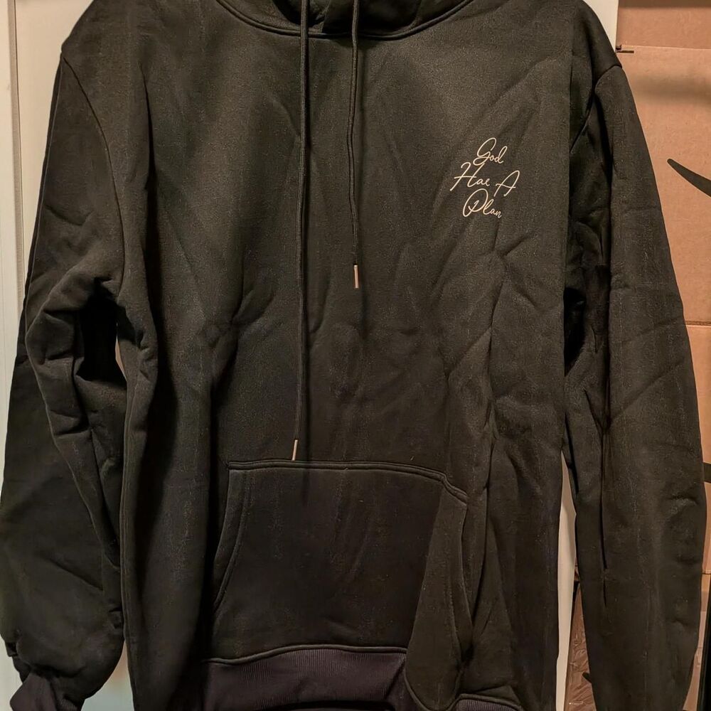 Black hoodie with white cursive text reading 'God Has A Plan'